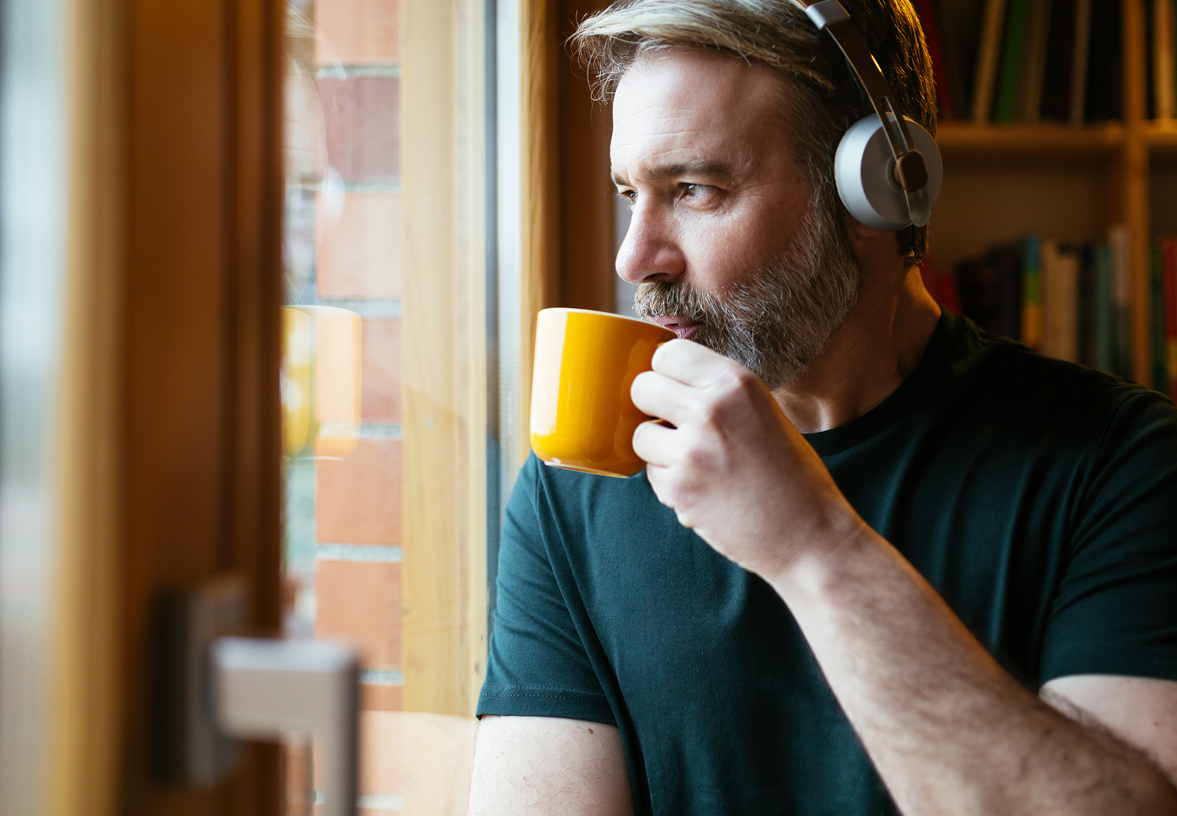 man with headphones drinking coffee and staring out a window